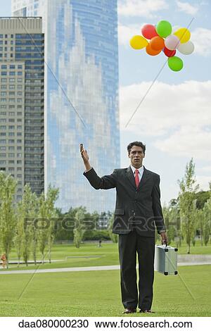 Businessman releasing bunch of balloons into air, looking disappointed View Large Photo Image Stock Image - Businessman releasing bunch of balloons into air, looking disappointed. Fotosearch