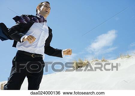 Businessman running across sand dune, low angle view View Large Photo Image Stock Photograph - Businessman running across sand dune, low angle view. Fotosearch
