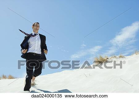 Businessman running across sand dune, low angle view View Large Photo Image Stock Photography - Businessman running across sand dune, low angle view. Fotosearch