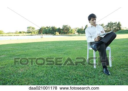 Businessman sitting in chair, on lawn, reading newspaper and holding mug View Large Photo Image Stock Photo - Businessman sitting in chair, on lawn, reading newspaper and holding mug. Fotosearch