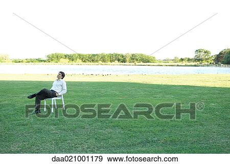 Stock Photo - Businessman sitting in chair on lawn, hands in pockets, looking up. Fotosearch