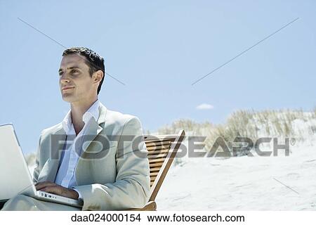 Businessman sitting in deck chair at beach, using laptop View Large Photo Image Picture - Businessman sitting in deck chair at beach, using laptop. Fotosearch