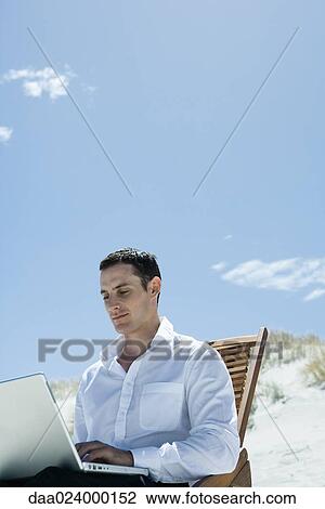 Businessman sitting in deck chair at beach, using laptop View Large Photo Image Stock Image - Businessman sitting in deck chair at beach, using laptop. Fotosearch