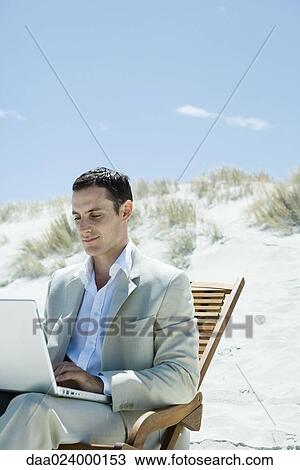Businessman sitting in deck chair at beach, using laptop View Large Photo Image Stock Image - Businessman sitting in deck chair at beach, using laptop. Fotosearch