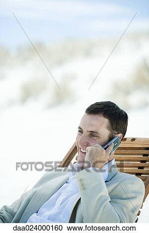 Businessman sitting in deck chair at beach, using cell phone View Large Photo Image Stock Image - Businessman sitting in deck chair at beach, using cell phone. Fotosearch