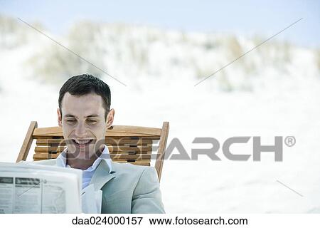 Businessman sitting in deck chair at beach, reading newspaper, smiling View Large Photo Image Stock Photo - Businessman sitting in deck chair at beach, reading newspaper, smiling. Fotosearch