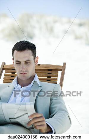 Stock Photo - Businessman sitting in deck chair at beach, reading newspaper. Fotosearch