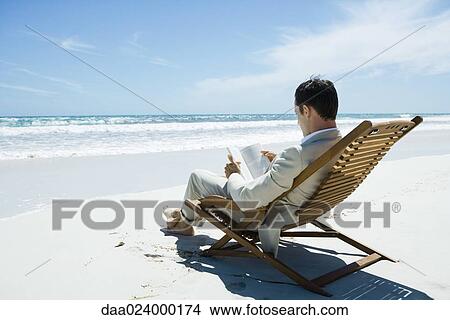 Businessman sitting in deckchair on beach, reading book View Large Photo Image Picture - Businessman sitting in deckchair on beach, reading book. Fotosearch