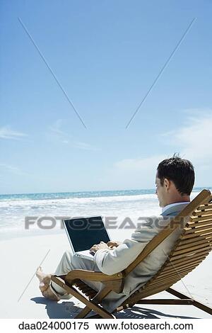 Businessman sitting in deckchair on beach, using laptop View Large Photo Image Stock Photography - Businessman sitting in deckchair on beach, using laptop. Fotosearch