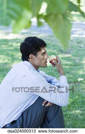 Businessman sitting on grass, eating apple, side view View Large Photo Image Stock Image - Businessman sitting on grass, eating apple, side view. Fotosearch