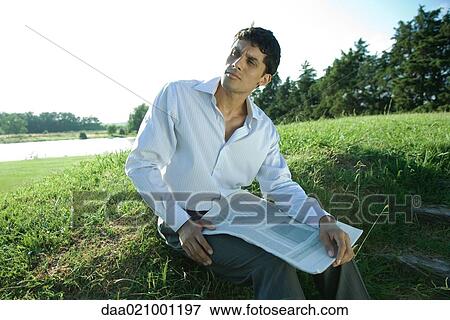 Stock Photo - Businessman sitting on grass, holding newspaper. Fotosearch