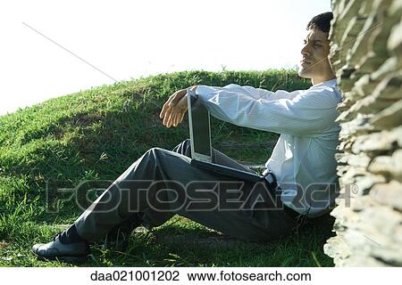 Businessman sitting on ground, holding laptop, looking away View Large Photo Image Stock Image - Businessman sitting on ground, holding laptop, looking away. Fotosearch