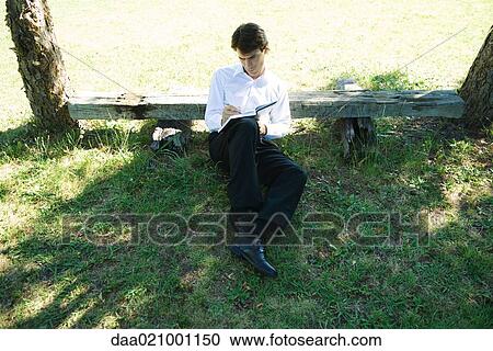 Businessman sitting on ground, leaning against bench, writing View Large Photo Image Stock Image - Businessman sitting on ground, leaning against bench, writing. Fotosearch