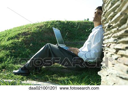 Businessman sitting on ground, using laptop, looking up View Large Photo Image Stock Image - Businessman sitting on ground, using laptop, looking up. Fotosearch