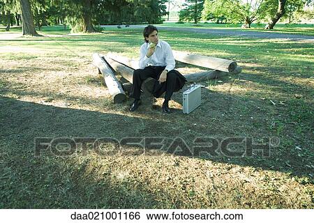 Businessman sitting on logs, eating an apple, looking away View Large Photo Image Stock Photograph - Businessman sitting on logs, eating an apple, looking away. Fotosearch