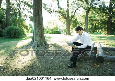Businessman sitting on logs, reading newspaper View Large Photo Image Picture - Businessman sitting on logs, reading newspaper. Fotosearch
