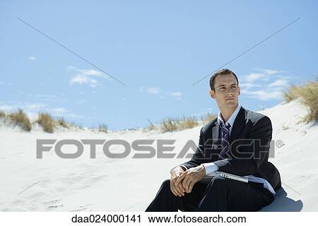 Businessman sitting on sand dune, closed laptop on lap View Large Photo Image Stock Image - Businessman sitting on sand dune, closed laptop on lap. Fotosearch