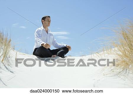 Businessman sitting on sand dune, meditating View Large Photo Image Stock Image - Businessman sitting on sand dune, meditating. Fotosearch