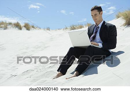 Businessman sitting on sand dune, using laptop View Large Photo Image Stock Image - Businessman sitting on sand dune, using laptop. Fotosearch