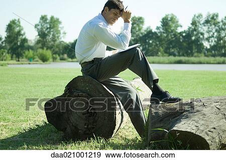 Businessman sitting on tree trunk, working View Large Photo Image Stock Photo - Businessman sitting on tree trunk, working. Fotosearch