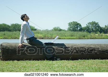Businessman sitting on tree trunk with laptop, looking up View Large Photo Image Stock Image - Businessman sitting on tree trunk with laptop, looking up. Fotosearch