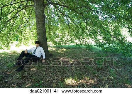 Stock Image - Businessman sitting under tree. Fotosearch