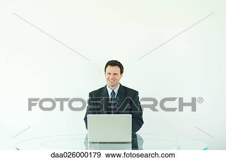 Businessman sitting, using laptop computer, smiling at camera View Large Photo Image Stock Photo - Businessman sitting, using laptop computer, smiling at camera. Fotosearch