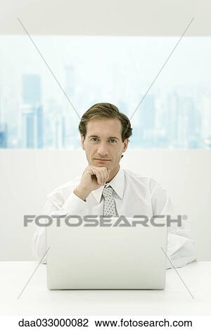 Businessman sitting with laptop computer, holding head, smiling at camera View Large Photo Image Stock Image - Businessman sitting with laptop computer, holding head, smiling at camera. Fotosearch