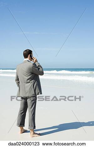 Businessman standing barefoot on beach, using cell phone View Large Photo Image Stock Image - Businessman standing barefoot on beach, using cell phone. Fotosearch
