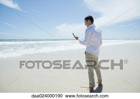 Businessman standing barefoot on beach, holding up cell phone View Large Photo Image Stock Image - Businessman standing barefoot on beach, holding up cell phone. Fotosearch