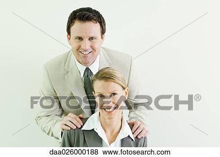 Stock Photo - Businessman standing behind female associate with his hands on her shoulders, both smiling at camera. Fotosearch