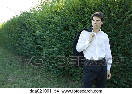 Businessman standing by hedge, holding jacket over shoulder, looking away View Large Photo Image Picture - Businessman standing by hedge, holding jacket over shoulder, looking away. Fotosearch