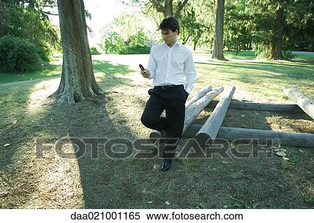 Businessman standing by logs, looking at cell phone View Large Photo Image Stock Photography - Businessman standing by logs, looking at cell phone. Fotosearch