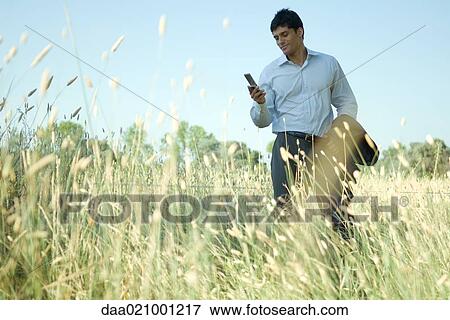 Stock Photo - Businessman standing in field, looking at cell phone. Fotosearch