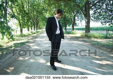 Stock Photography - Businessman standing in rural road, looking down. Fotosearch