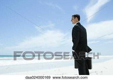 Businessman standing on beach, looking at view, smiling View Large Photo Image Stock Photo - Businessman standing on beach, looking at view, smiling. Fotosearch