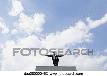 Businessman standing on concrete structure with arms outstretched, low angle view View Large Photo Image Stock Image - Businessman standing on concrete structure with arms outstretched, low angle view. Fotosearch