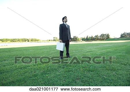 Businessman standing on lawn, holding briefcase View Large Photo Image Stock Photo - Businessman standing on lawn, holding briefcase. Fotosearch