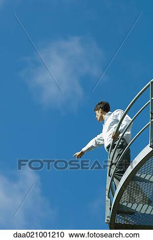 Businessman standing on metal balcony, pointing to distance, low angle view, blue sky in background View Large Photo Image Stock Image - Businessman standing on metal balcony, pointing to distance, low angle view, blue sky in background. Fotosearch