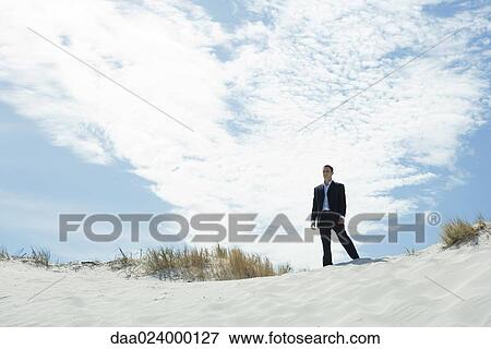Businessman standing on sand dune, low angle view View Large Photo Image Stock Photo - Businessman standing on sand dune, low angle view. Fotosearch