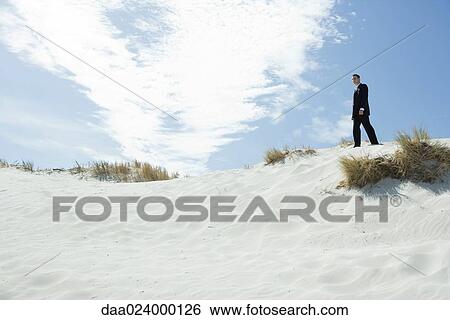 Businessman standing on sand dune, low angle view View Large Photo Image Stock Photograph - Businessman standing on sand dune, low angle view. Fotosearch