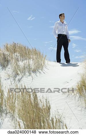 Stock Photo - Businessman standing on sand dune, looking away. Fotosearch
