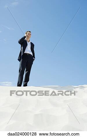 Businessman standing on sand, using cell phone, low angle view View Large Photo Image Stock Photo - Businessman standing on sand, using cell phone, low angle view. Fotosearch
