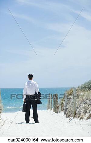 Businessman standing on sandy path leading to ocean, rear view View Large Photo Image Picture - Businessman standing on sandy path leading to ocean, rear view. Fotosearch