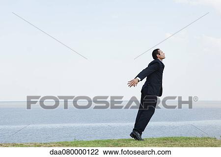 Businessman standing on tiptoe by sea, taking deep breath View Large Photo Image Stock Image - Businessman standing on tiptoe by sea, taking deep breath. Fotosearch