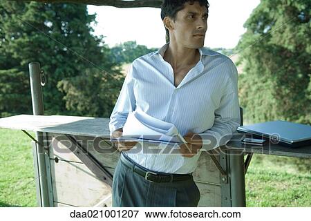 Stock Photo - Businessman standing outdoors, holding documents. Fotosearch