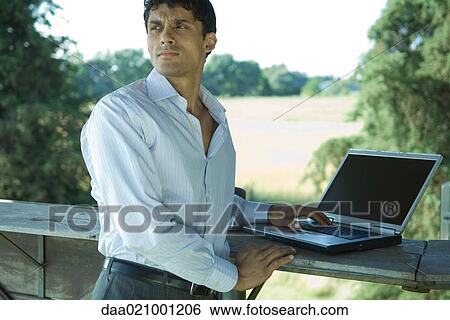 Businessman standing outdoors, with laptop View Large Photo Image Stock Photograph - Businessman standing outdoors, with laptop. Fotosearch