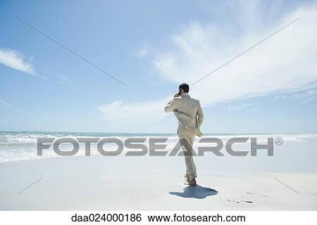Businessman walking barefoot on beach, using cell phone View Large Photo Image Stock Photograph - Businessman walking barefoot on beach, using cell phone. Fotosearch