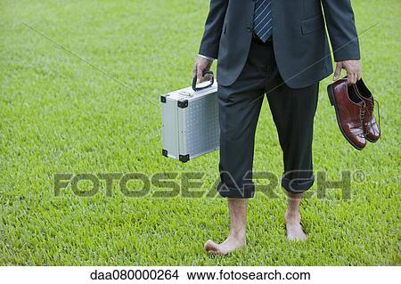 Businessman walking barefoot on grass carrying shoes and briefcase View Large Photo Image Picture - Businessman walking barefoot on grass carrying shoes and briefcase. Fotosearch