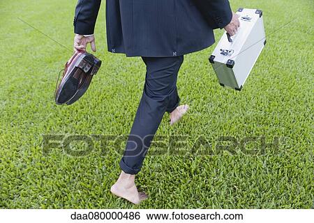 Businessman walking barefoot on grass carrying shoes and briefcase, cropped View Large Photo Image Stock Photograph - Businessman walking barefoot on grass carrying shoes and briefcase, cropped. Fotosearch